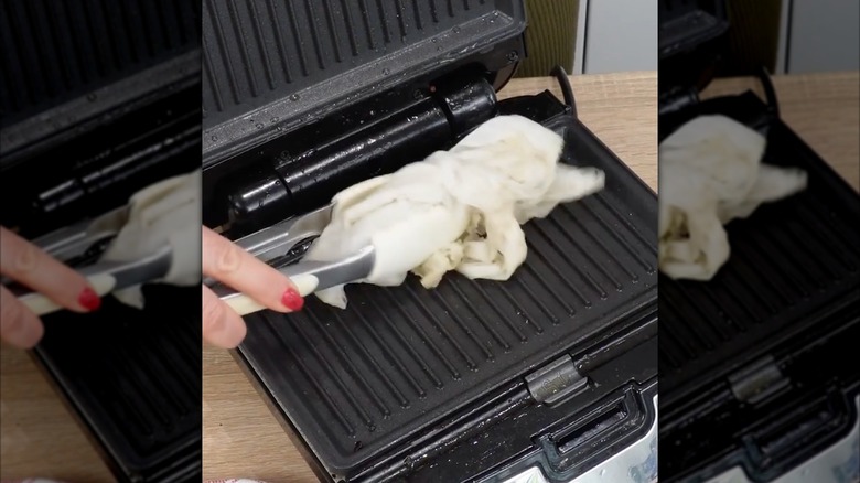 Screenshot of person cleaning panini grill with wet paper towels
