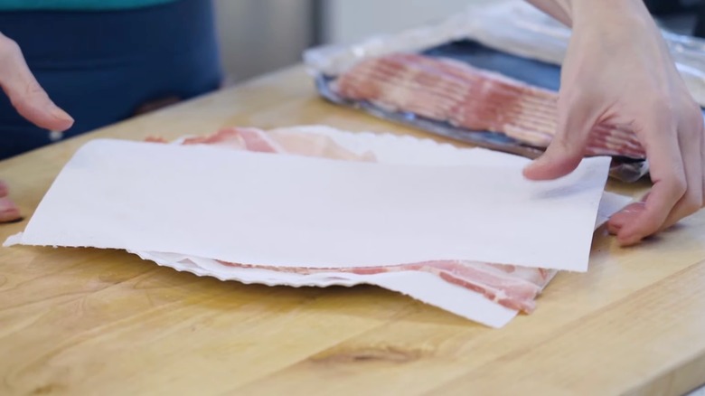 person placing paper towels over bacon plate