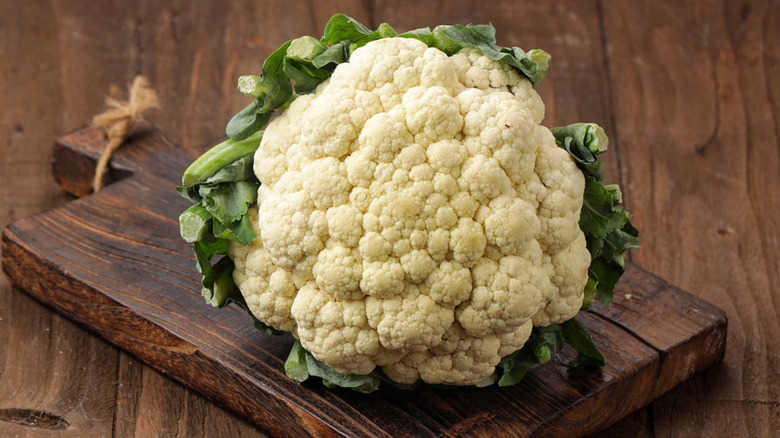 A fresh head of cauliflower sitting on a wooden cutting board.