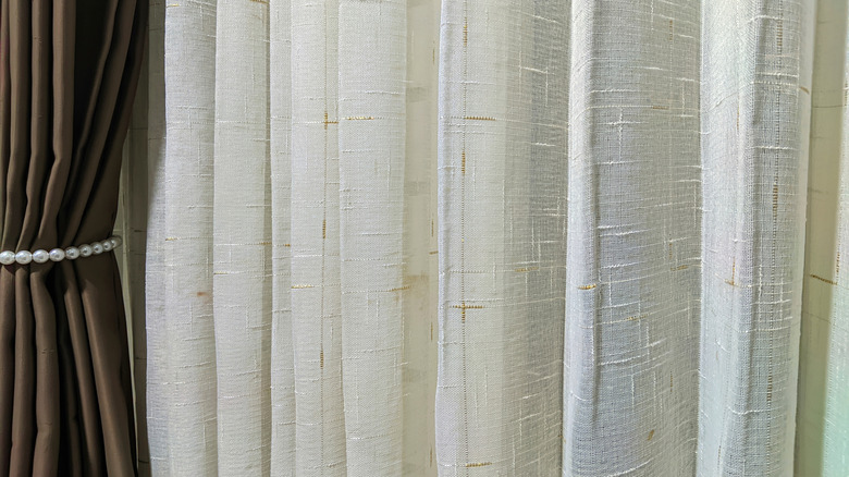 a set of pleated curtains is held with a tie back in front of a softer see through curtain