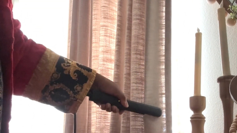 a woman uses a flat iron to create sharp pleats in her pleated curtains