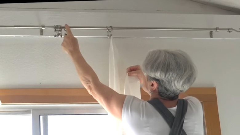 a woman hangs a flat panel curtain evenly on curtain rings