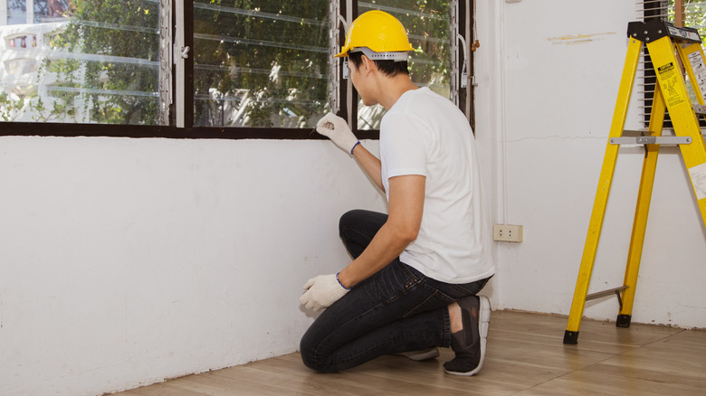 A person in a yellow hard hat inspecting a windowsill for signs of termites.