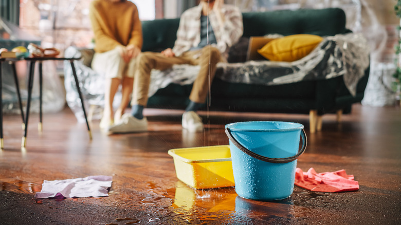 Buckets on floor to catch drips from leak and couple in the background on the phone