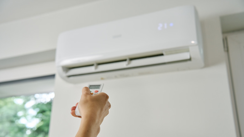 Hand holding a remote to adjust the setting on a wall-mounted ductless AC system