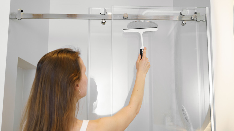 Woman using a squeegee on a glass shower divider to remove moisture