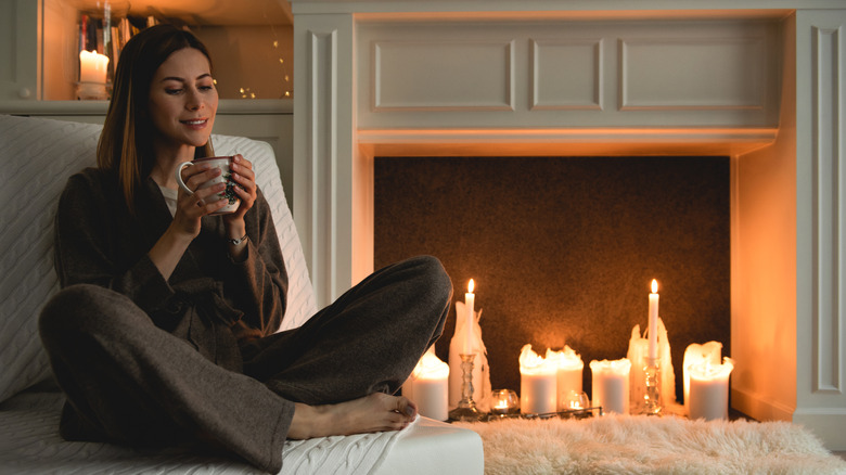Woman sitting next to a fireplace with candles in it