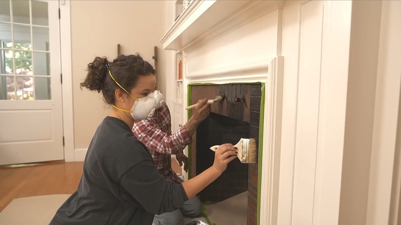 Man and woman painting the brick surround of a fireplace