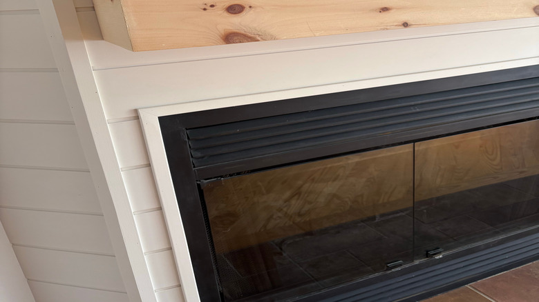 New natural wood mantel installed against a white wall above the fireplace