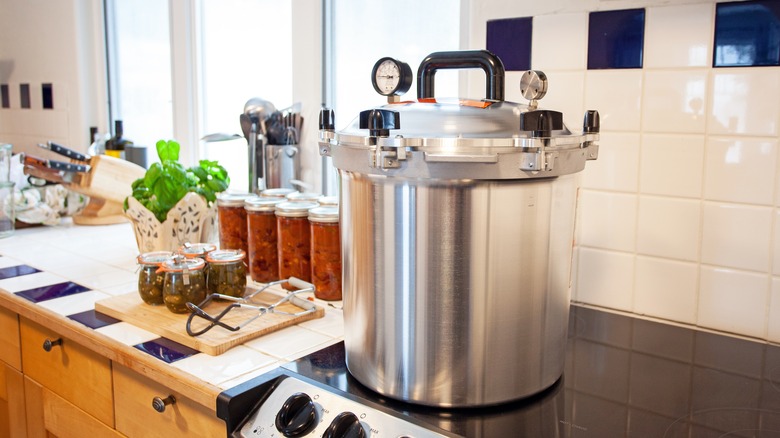 Pressure canner on stove top with canned food on counter