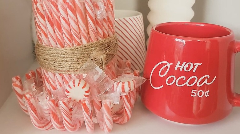 Battery-operated pillar candle covered with upside-down candy canes tied with twine next to a hot cocoa mug