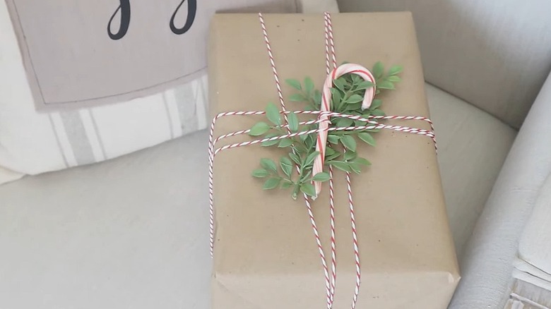 Gift wrapped in brown paper with a candy cane, greenery, and red and white twine