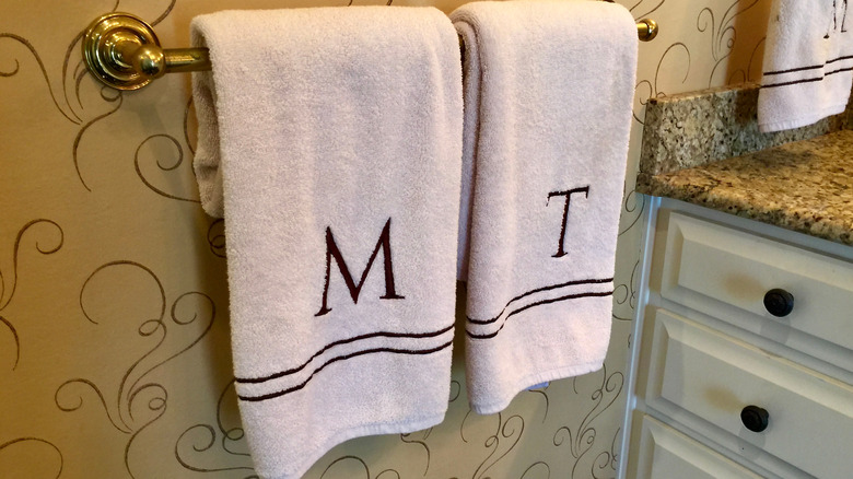 Monogrammed M and T towels hanging on a towel rod in a bathroom.