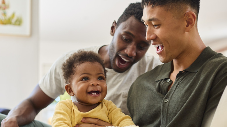 Couple Playing With Baby Sitting On Sofa At Home Together