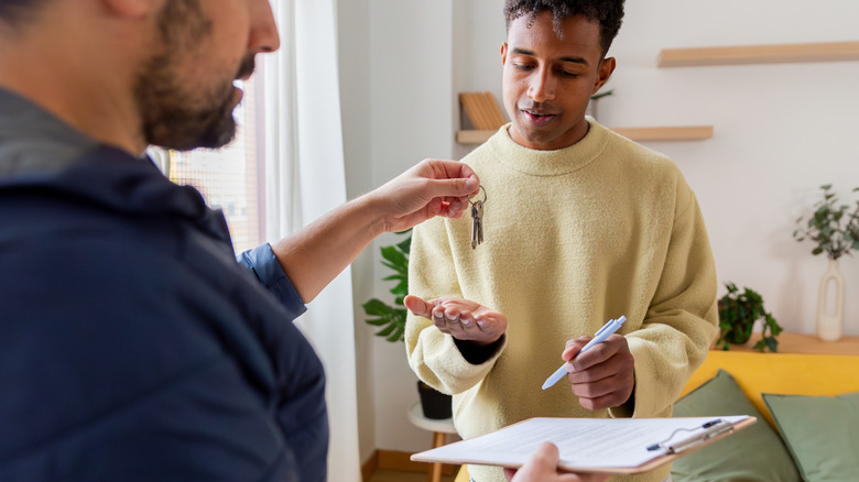 Landlord handing house keys to a young man signing a rental contract for a new home