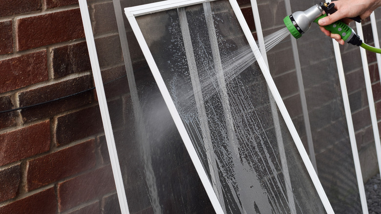 Closeup hand of a person washing dirty window screens with water hose