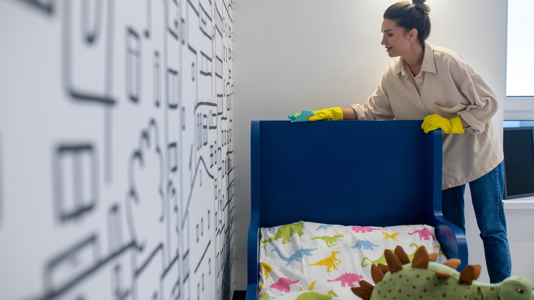 Woman wearing gloves and dusting the top of a blue kids' bed
