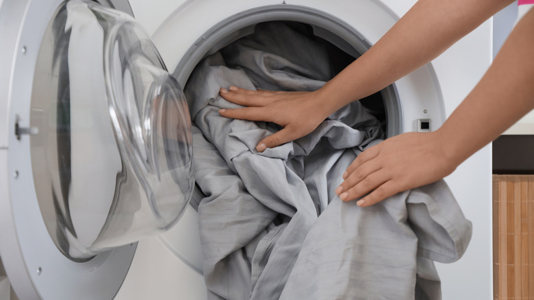 Person pushing gray sheets into an open front-loading washing machine