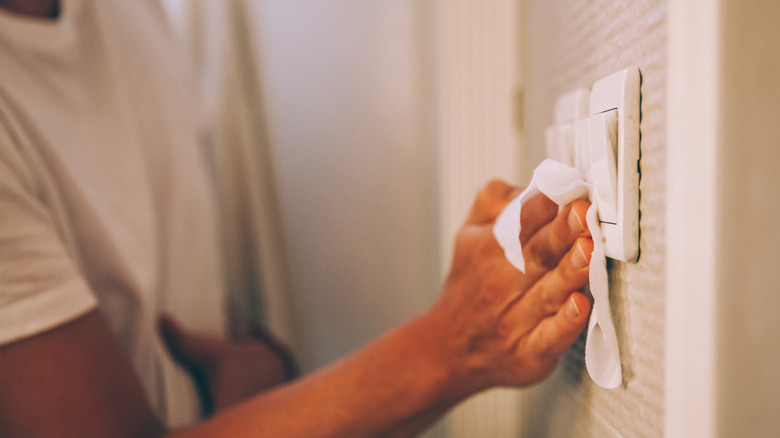 Hand wiping wall light switch with cloth.
