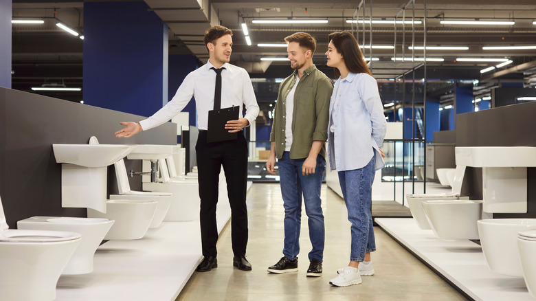 Store salesman marketing toilets to a couple in a store