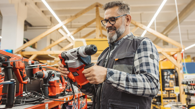 A man looking at an orange power tool in a hardware store
