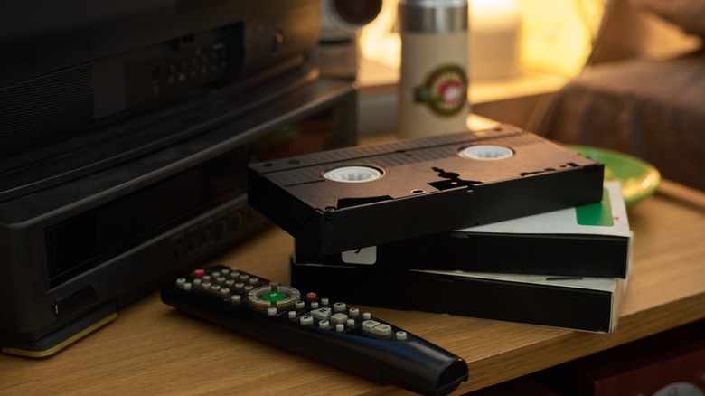 Close-up of several vintage VHS tapes stacked near remote control on wooden table