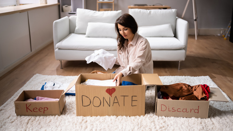 A woman sorting items into keep, donate, and discard boxes