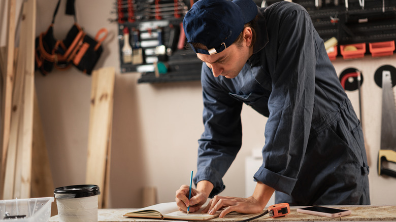 A man in a workshop making notes in a notebook