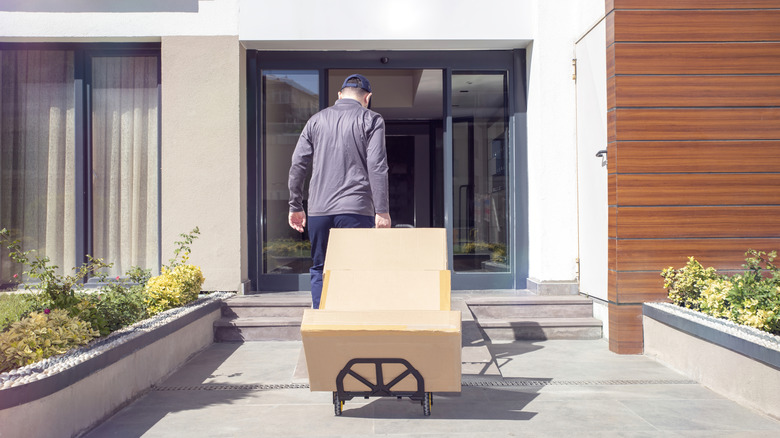 A delivery person wheeling a large item on a hand truck towards the door of a house