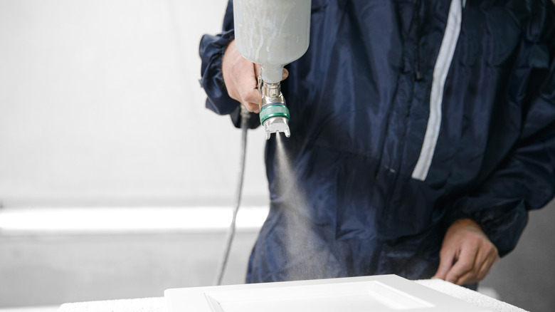 Close-up of somebody spraying a wooden cabinet door with a paint sprayer
