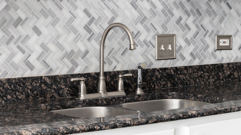 Patterned backsplash and countertop surrond a kitchen sink.