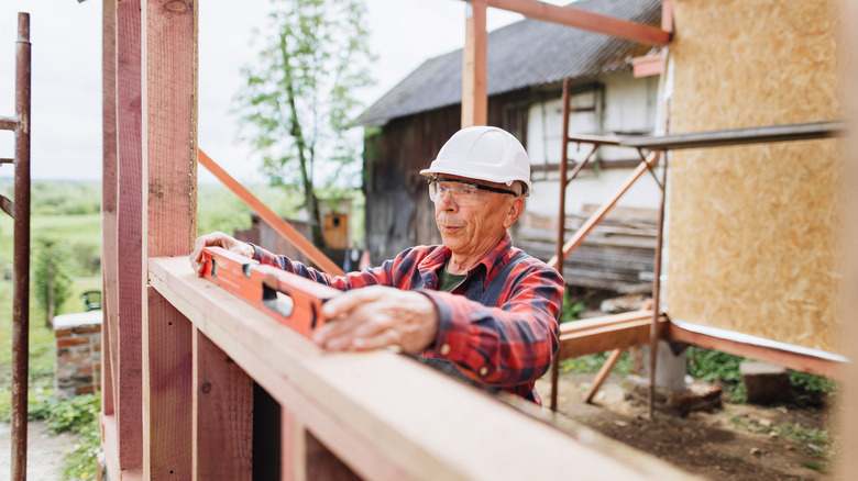 An older man in a red plaid shirt using a level to build.