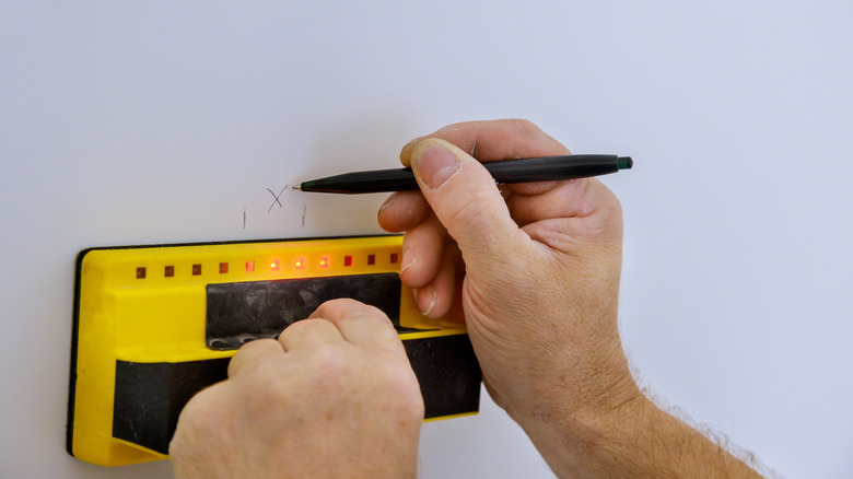 close up of a person's hands holding a stud finder against a wall