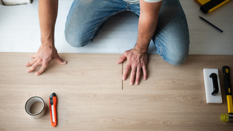 person installing laminate flooring with a utility knife on the floor in front of them