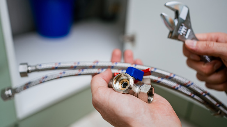 close up of a person's hands holding a wrench and water supply hoses