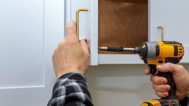 Close-up of a person installing gold-colored cabinet hand pulls