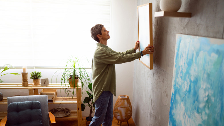 Woman hanging frame on wall of living area