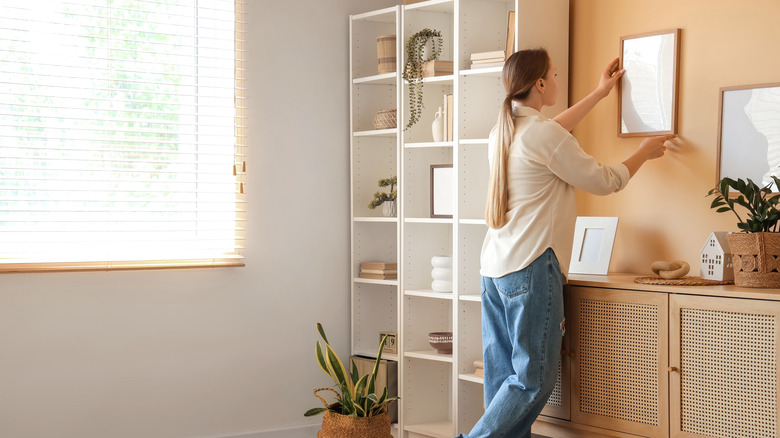 Woman hanging frame on wall in modern living room