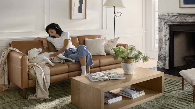 A woman sits on a Nomad sofa in brown leather from Burrow