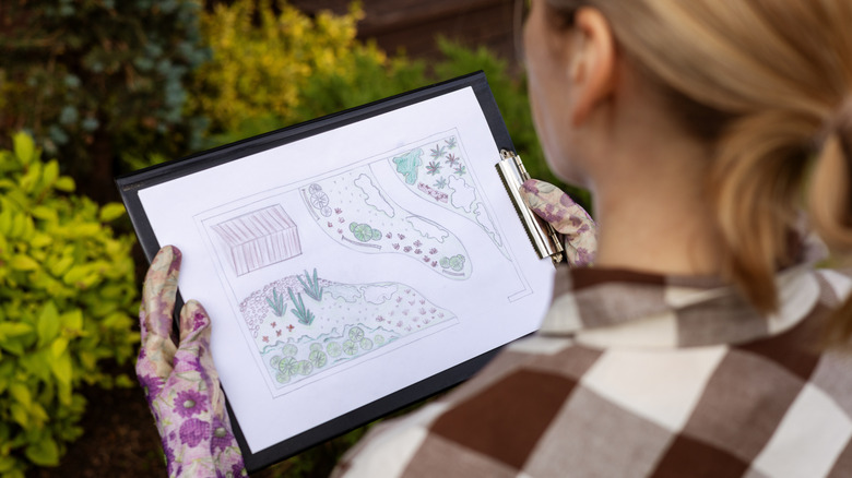 A woman stands outside looking at a hand-drawn map of her yard