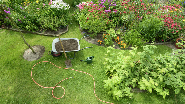 Various tools are shown near a garden and young trees, including wheelbarrow with compost, hose, spade and watering can.