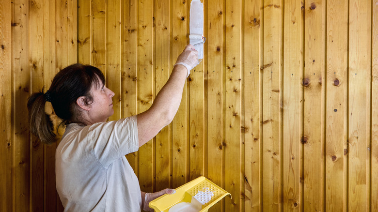Person starting to paint a wood wall with white paint