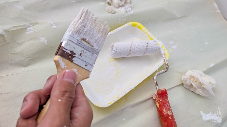 Person holding a paintbrush with white paint on it near a tray of white paint