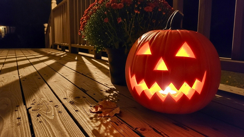 A carved pumpkin lit by a tea candle on a porch