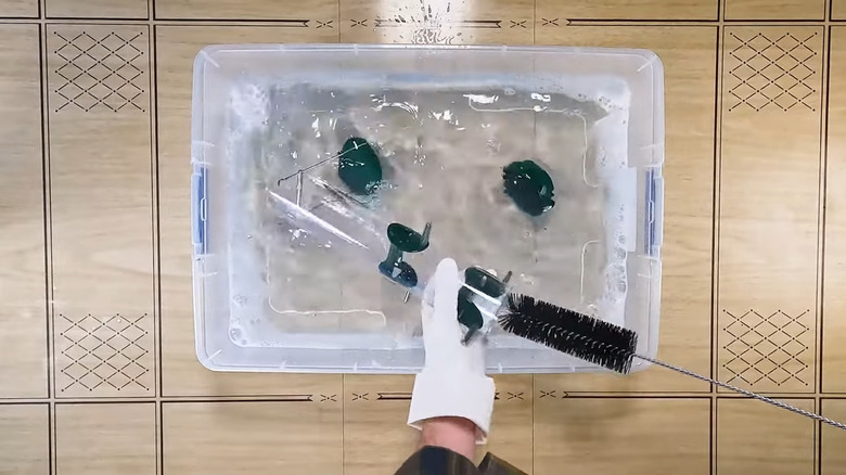 Person with gloved hands cleaning bird feeder in a solution of soap and water inside a plastic tub