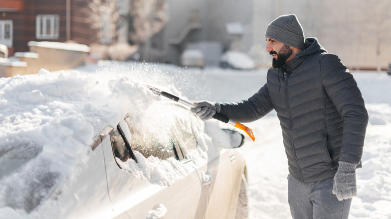 Man clearing the snow and ice off his car with a scraper