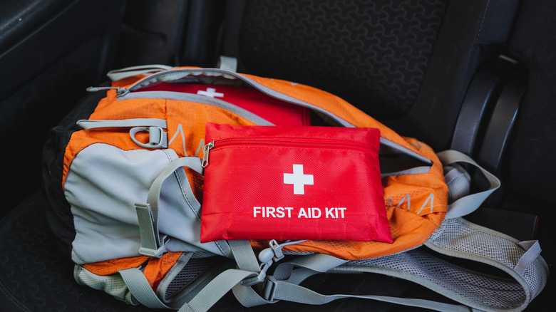 A first-aid kit on top of an orange backpack as part of a car emergency kit