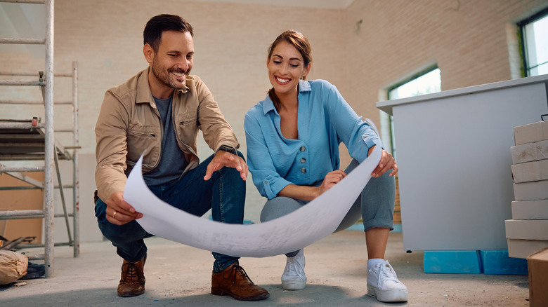 A couple looks at housing plans on the floor of their home