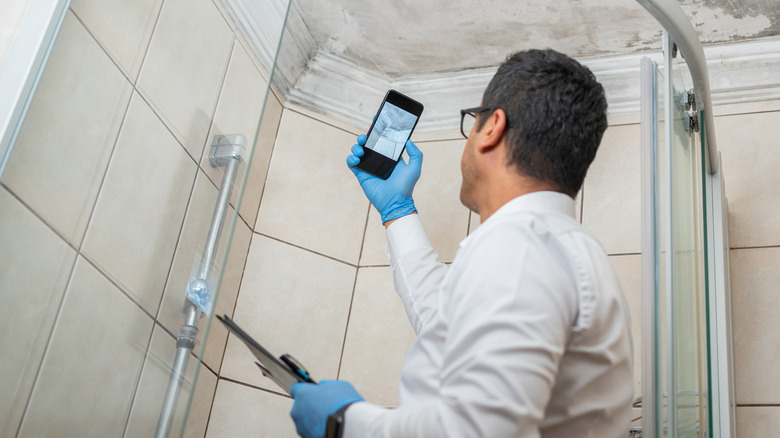 A man taking a photo of bathroom mold on his smartphone