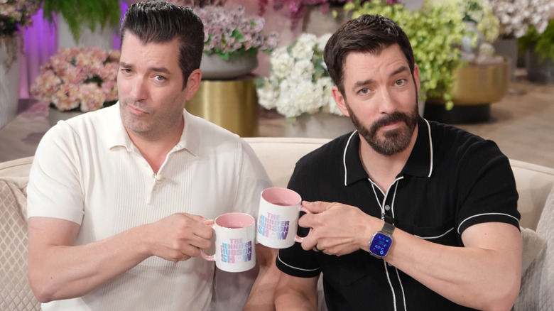 The Property Brothers posing with mugs on a talk show